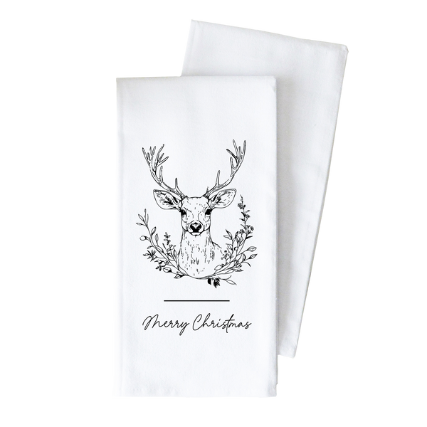 A white towel with a black and white illustration of a deer head surrounded by a wreath of leaves and branches, along with the text "Merry Christmas" printed on it.