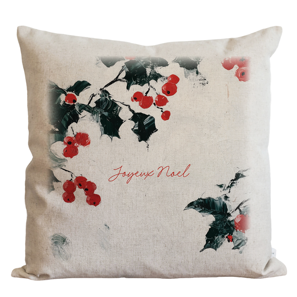 A white pillow with a design of red berries and green leaves, along with the text "Joyeux Noel" printed on it.