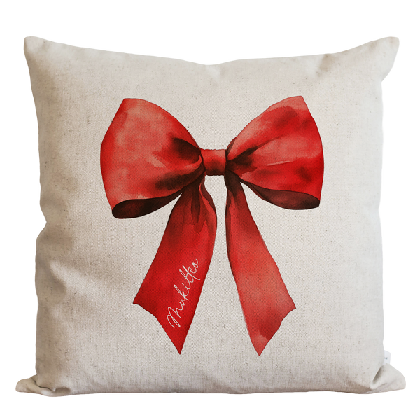 A white pillow with a red bow on it.