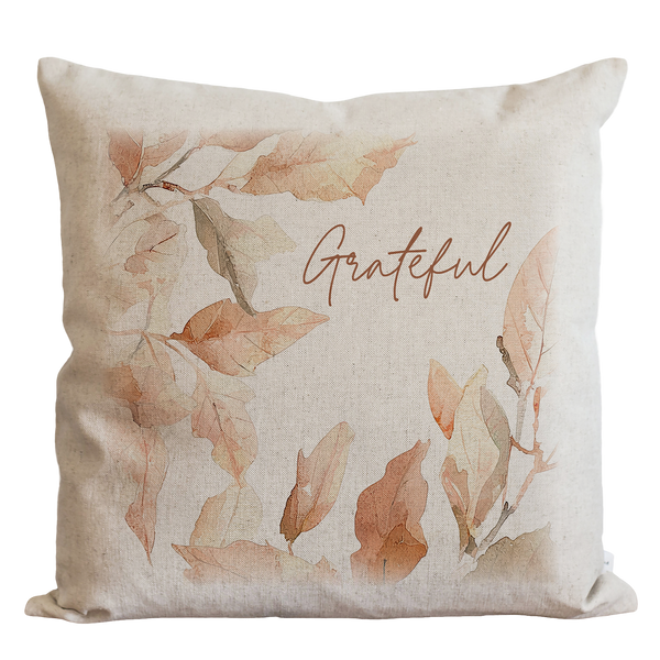 A beige pillow with a watercolor leaf design and the word "Grateful" written on it.