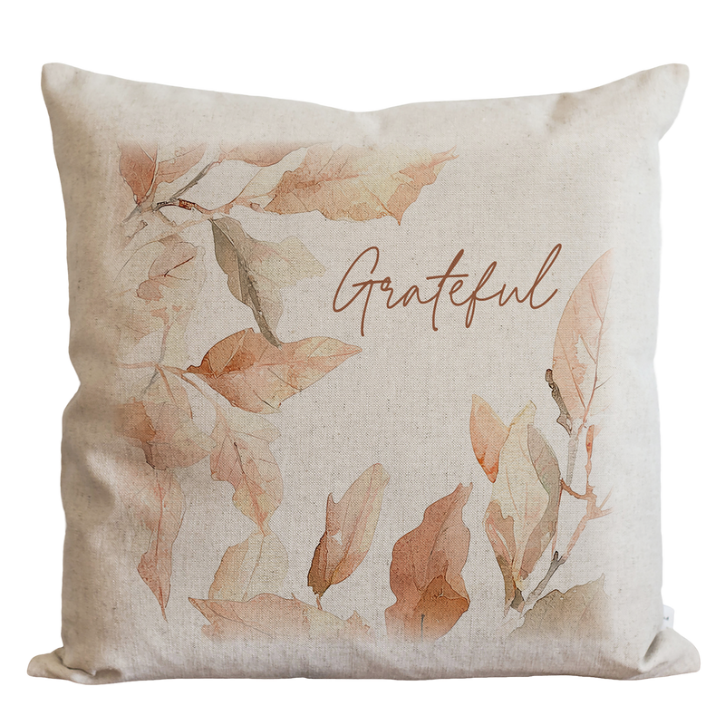 A beige pillow with a watercolor leaf design and the word "Grateful" written on it.