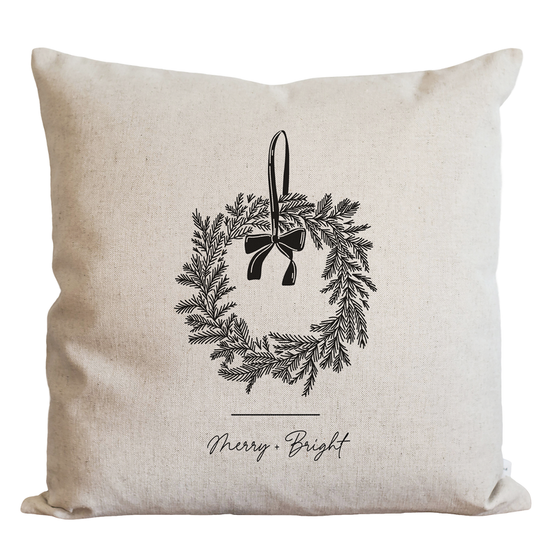 A beige pillow with a black wreath design and the text "Merry Bright" printed on it.