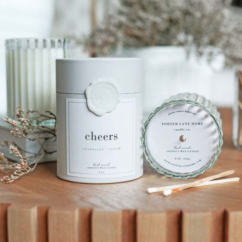 Candle labeled 'cheers' on a wooden surface with decorative elements.