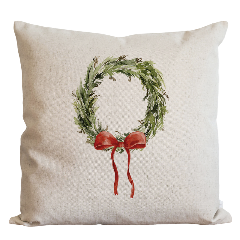 A white pillow with a wreath design and a red ribbon tied around it.