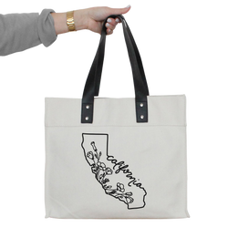 a woman's hand holding a white tote bag with a black outline of