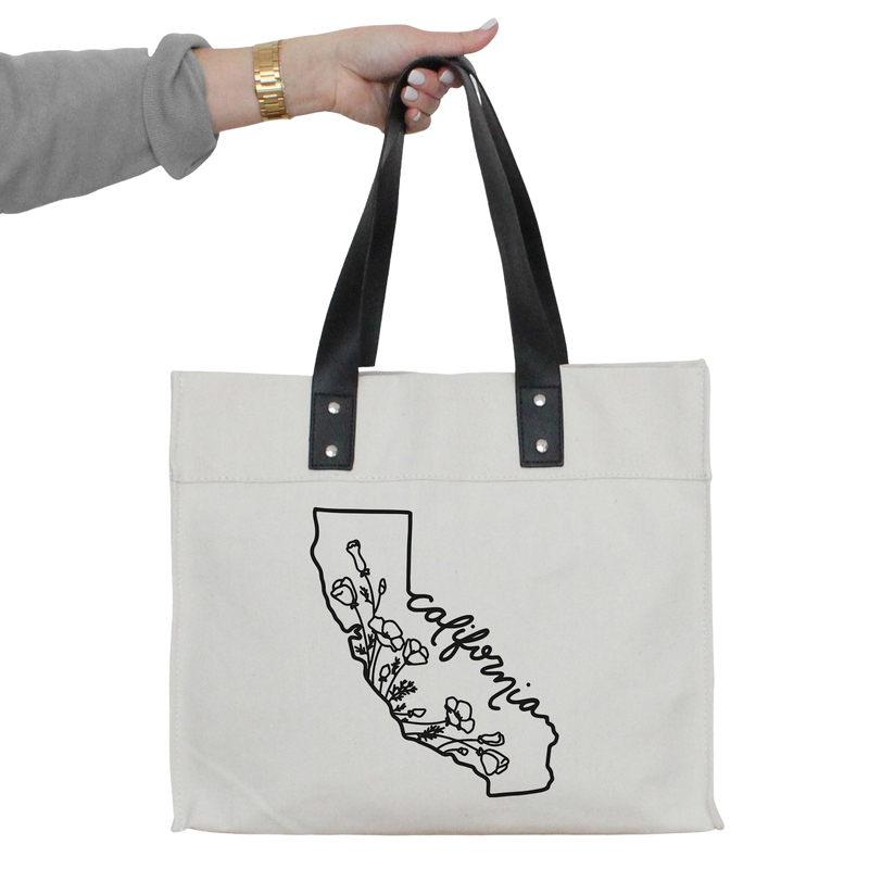 a woman's hand holding a white tote bag with a black outline of